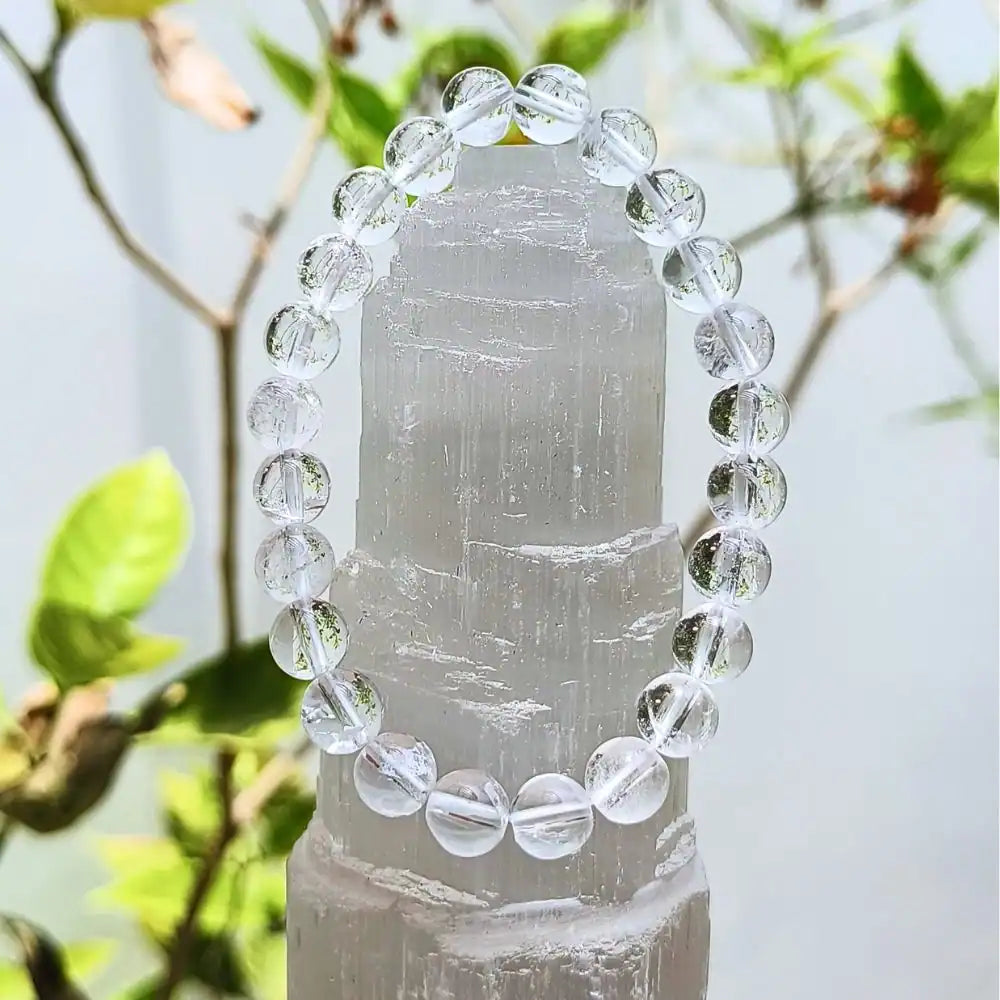 Clear quartz bracelet made of round polished beads displayed on a translucent crystal stand