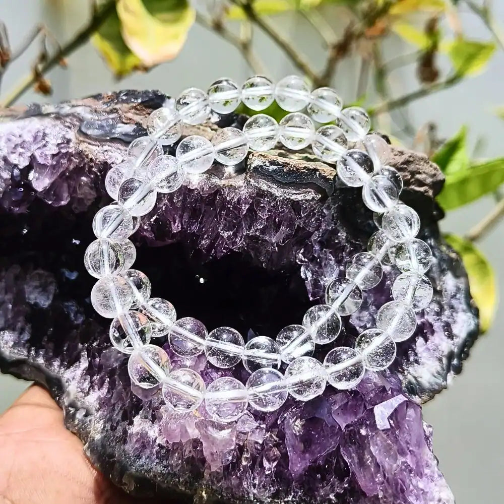 CRYSTCOP clear quartz bracelet with round beads placed on a purple amethyst crystal cluster