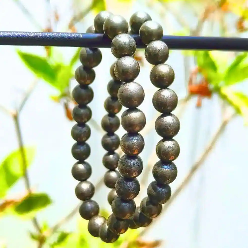 CRYSTCOP golden pyrite bracelet made of round metallic beads hanging on a rod outdoors