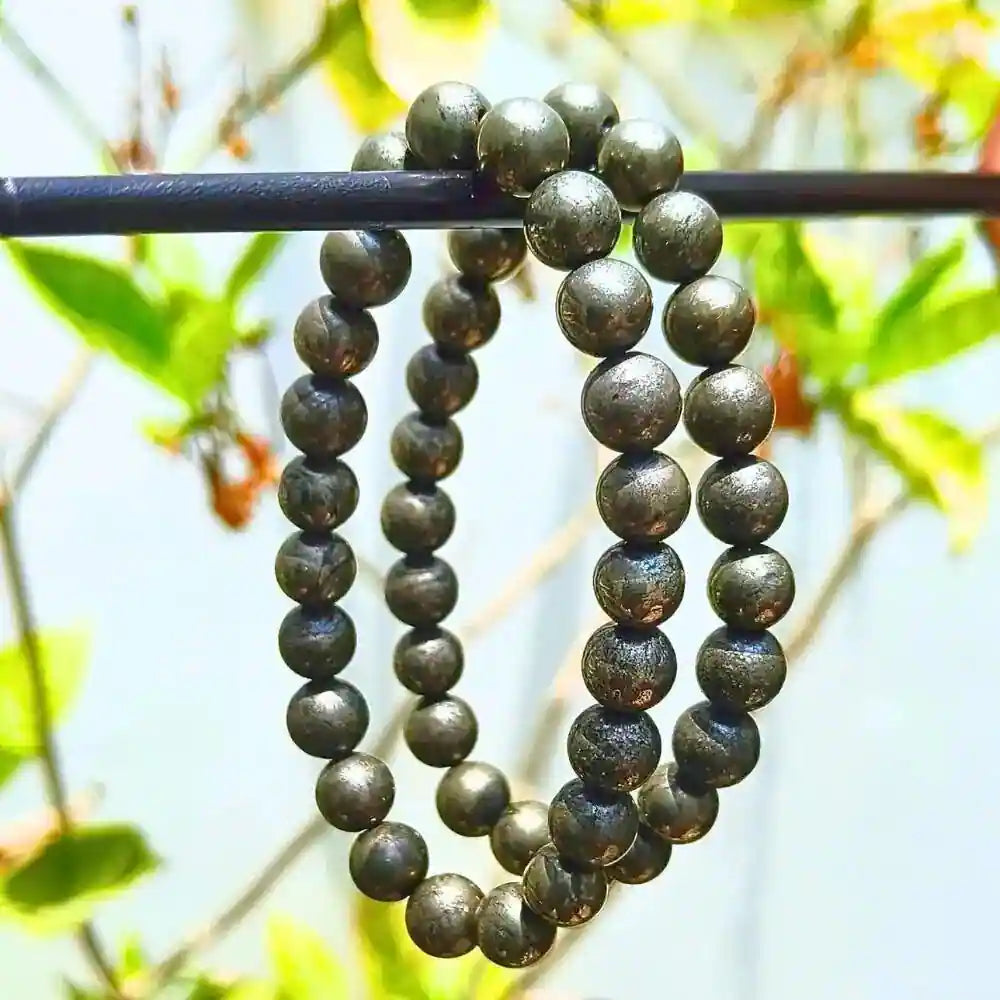 CRYSTCOP golden pyrite bracelet with polished round beads hanging on a black rod outdoors