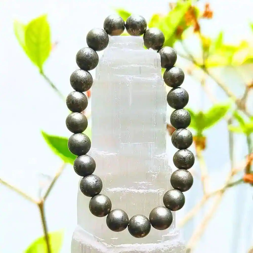 Golden pyrite bracelet with polished round beads displayed on a white crystal stand