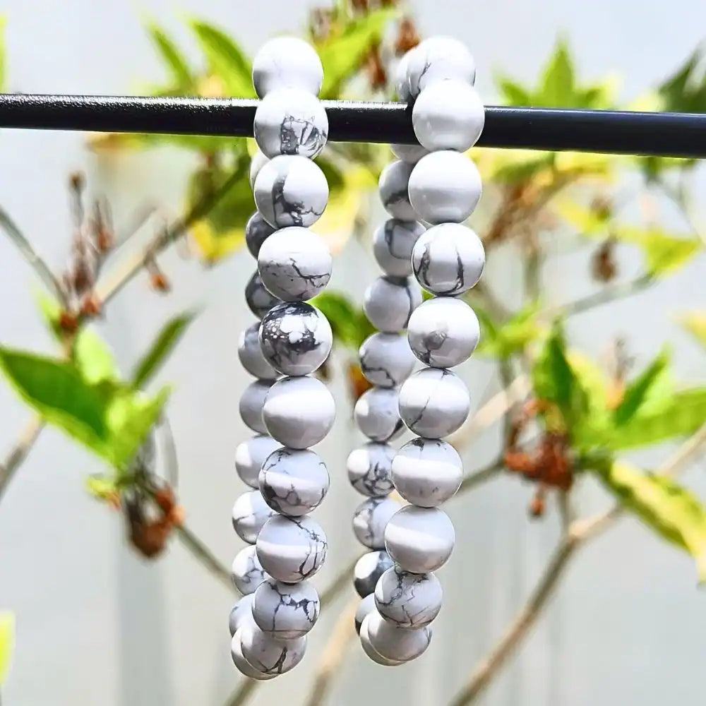 CRYSTCOP Howlite bracelet 8mm white beads with gray veins displayed outdoors on black rod