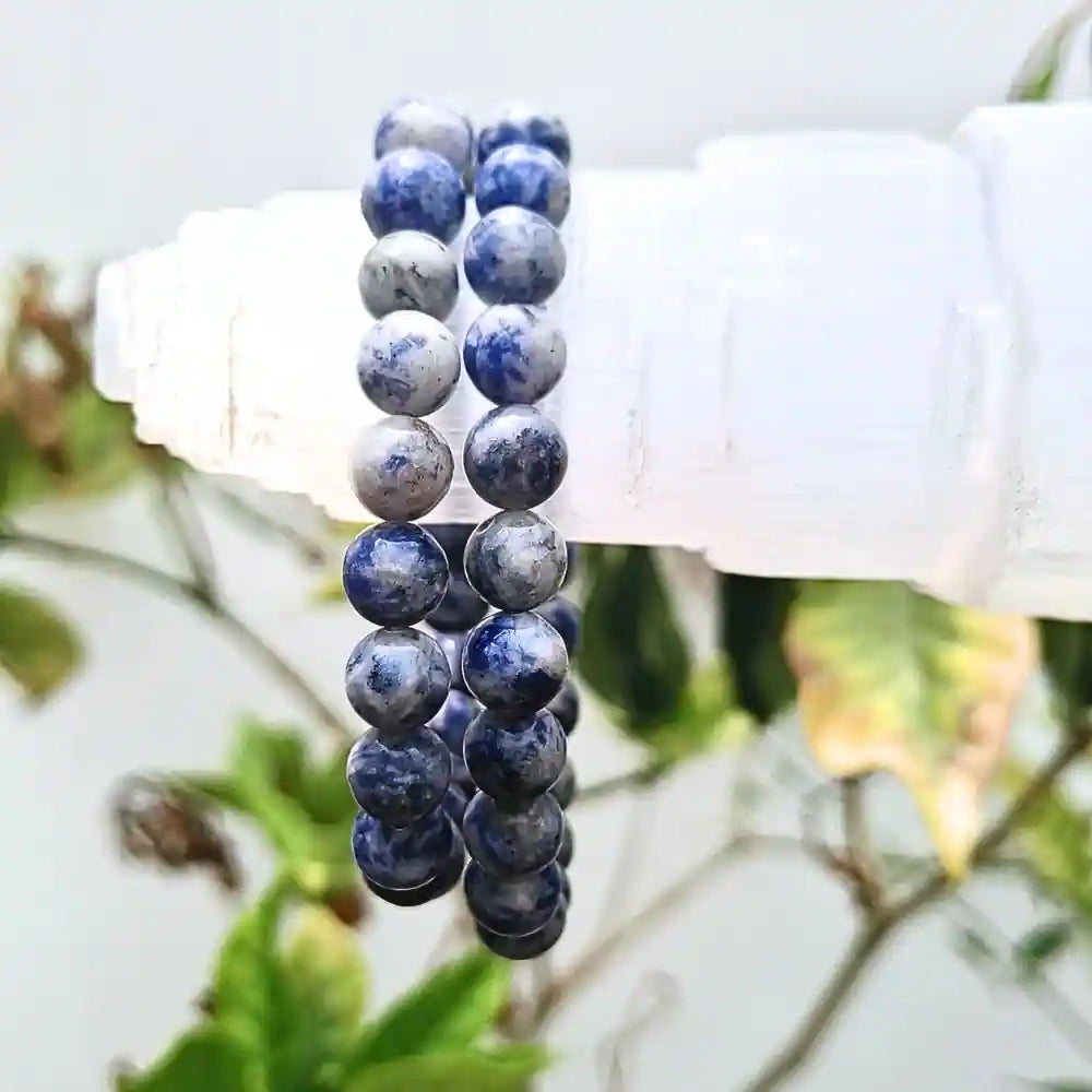 Natural sodalite beaded bracelet with deep blue and white marbled stones hanging on white crystal display
