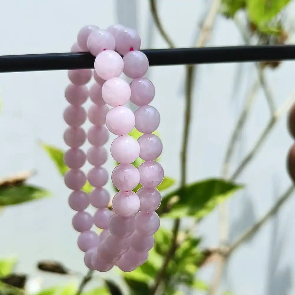 CRYSTCOP rose quartz energy jewelry bracelet with soft pink beads hanging on a black rod