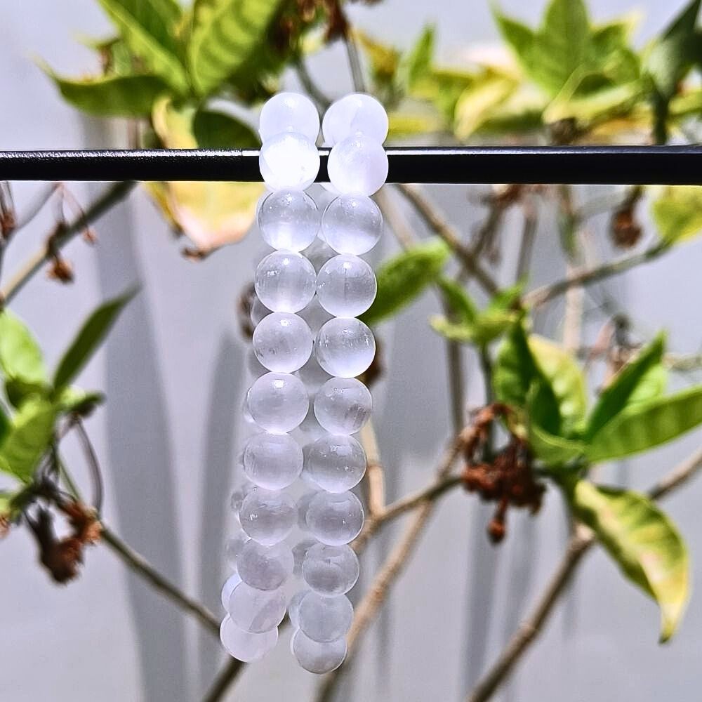 CRYSTCOP selenite bracelet 8mm with translucent white round beads hanging on a black rod outdoors