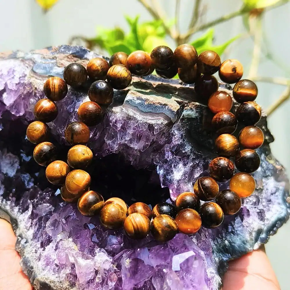 CRYSTCOP Tiger Eye bracelet 8mm with polished round beads displayed on purple amethyst crystal