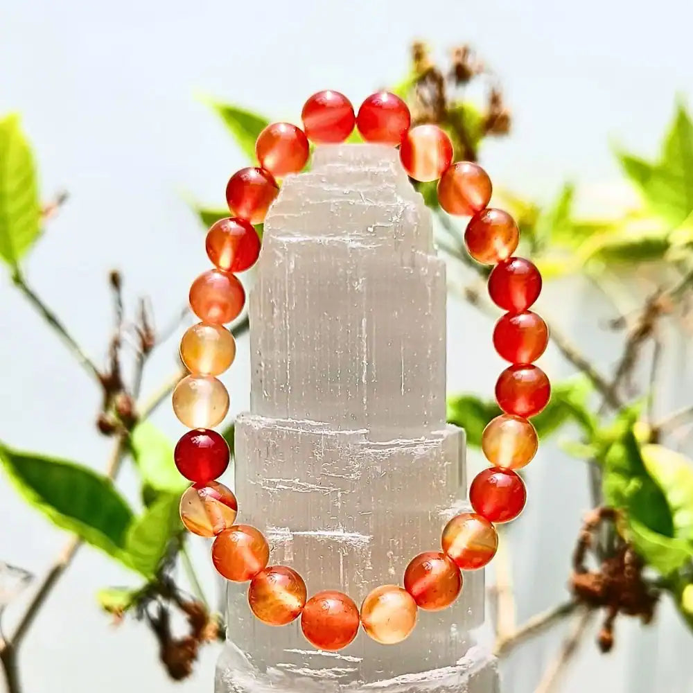 Carnelian bracelet 8mm round beads with orange and red hues displayed on a white crystal stand