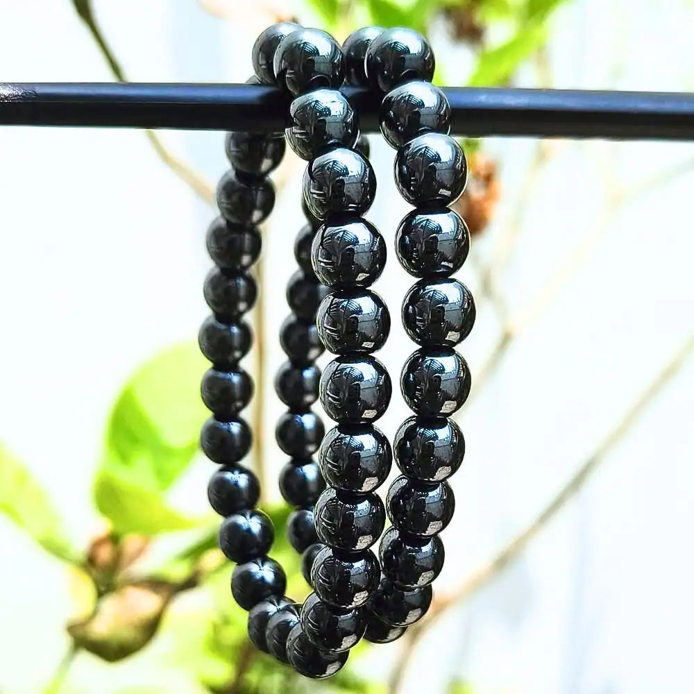 CRYSTCOP hematite bracelet 8mm with polished black beads hanging on a rod outdoors