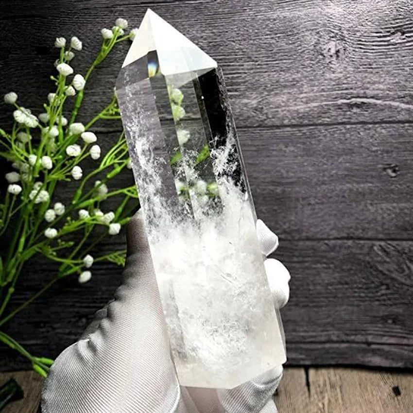 Hand holding a clear quartz crystal point with white flowers in the background to buy clear quartz online