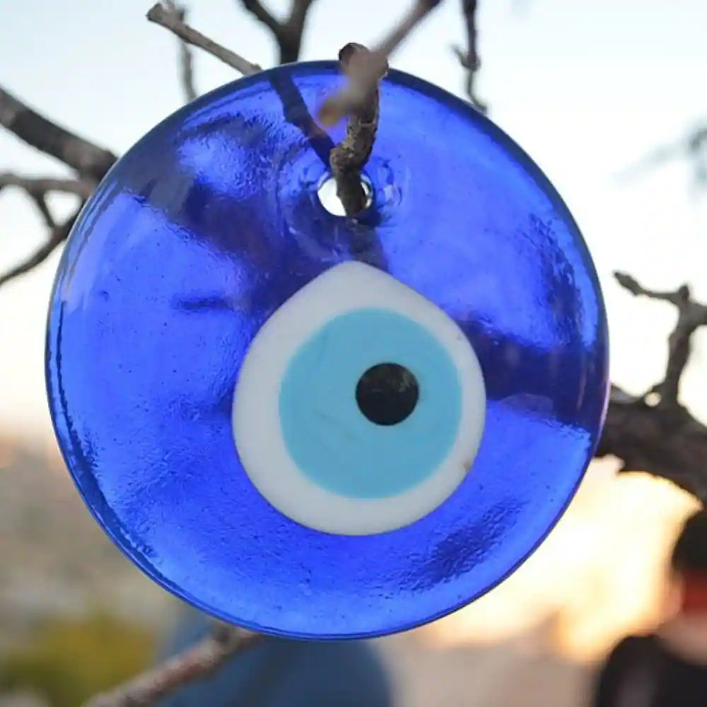 Close-up of a blue glass Protective Evil Eye charm hanging from a tree branch