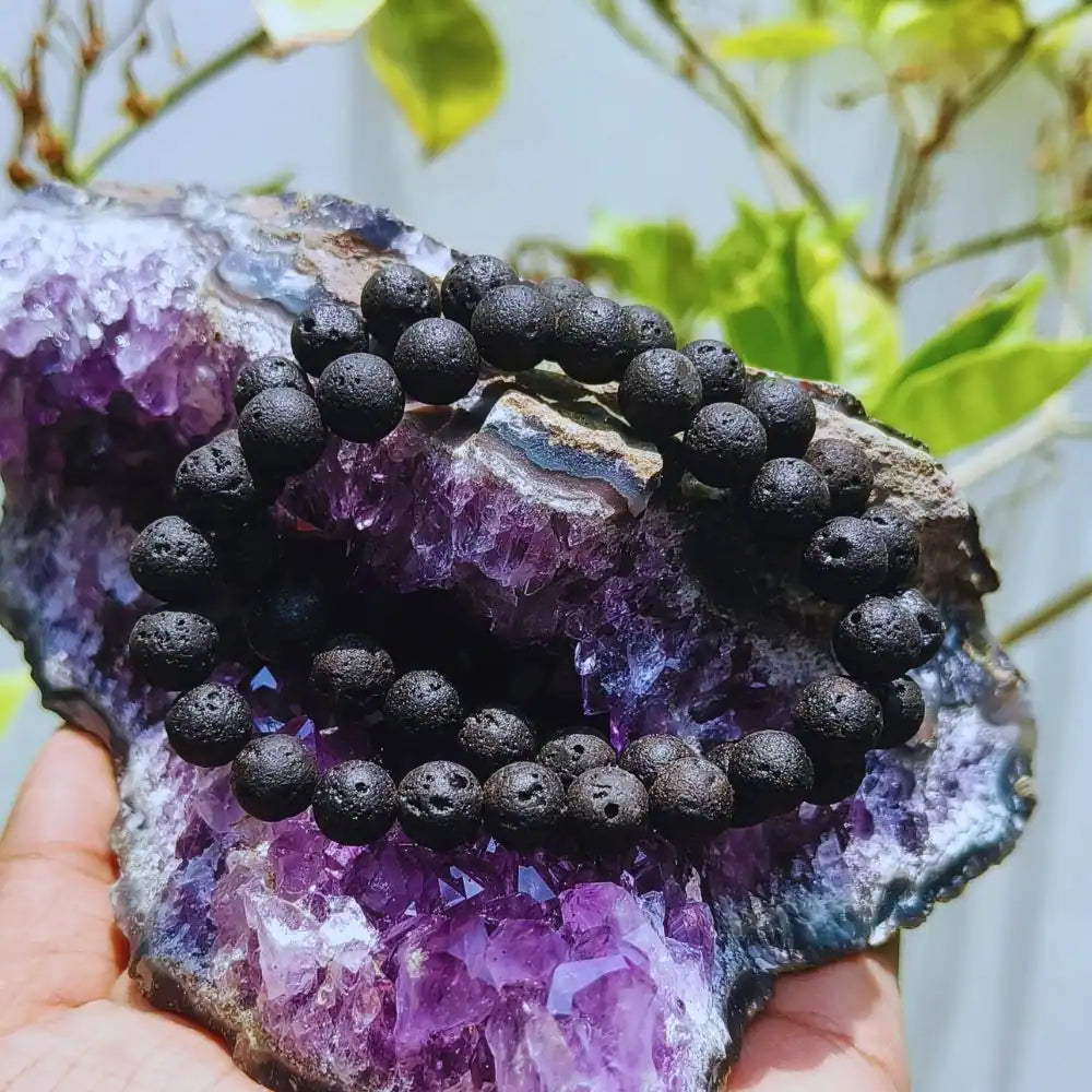 CRYSTCOP black lava bracelet with porous beads displayed on a purple amethyst crystal cluster