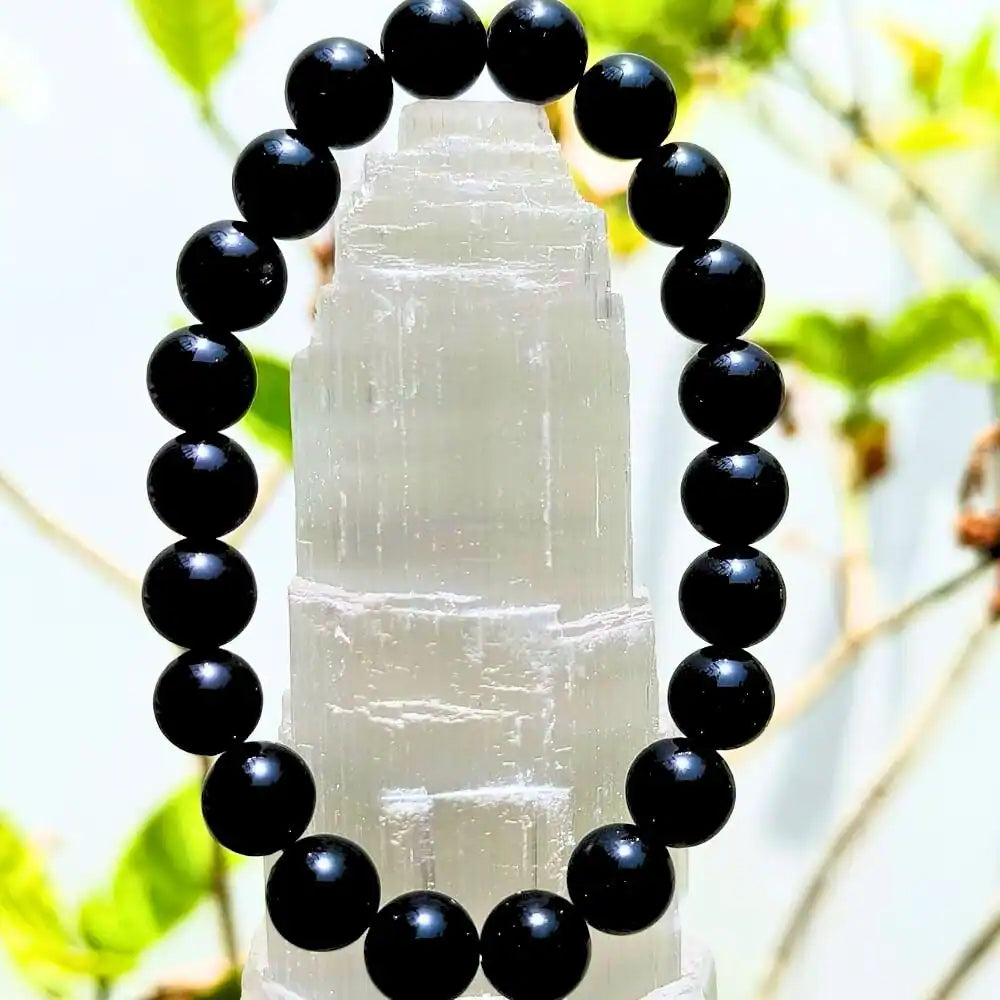 Black obsidian bracelet composed of polished black beads displayed on a white crystal stand