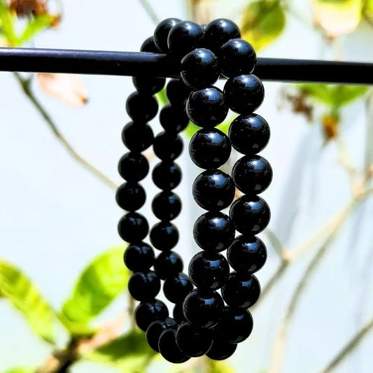 CRYSTCOP black obsidian bracelet made of polished round beads hanging on a black rod with a blurred natural background