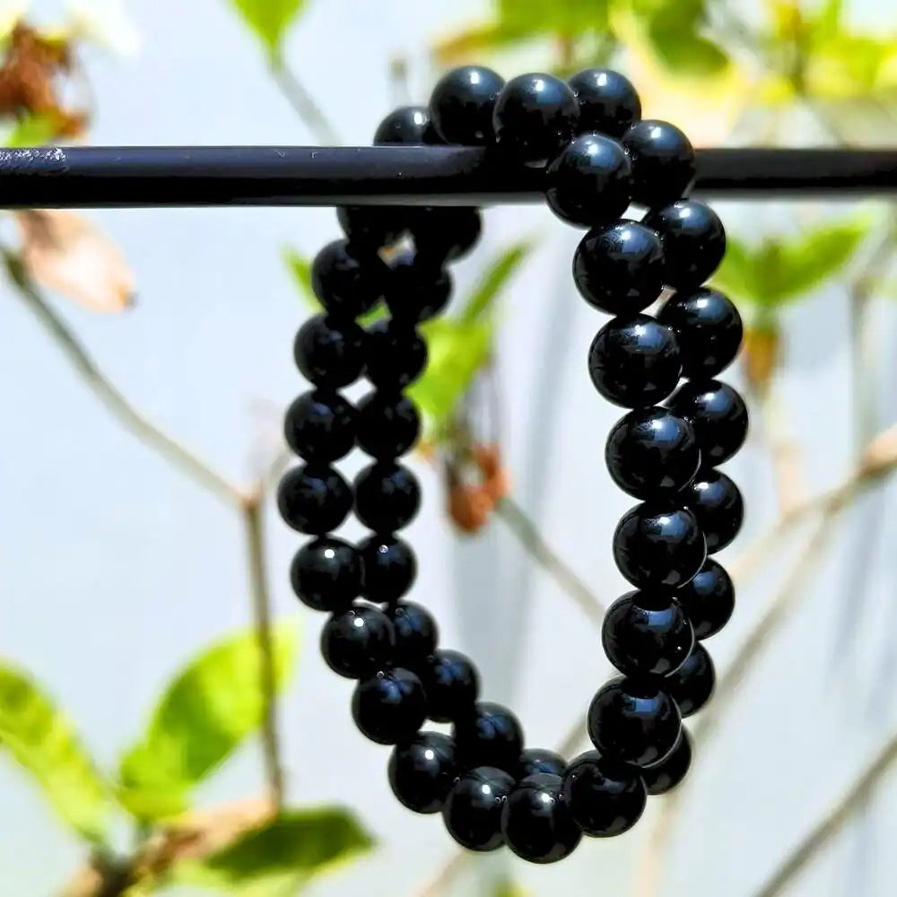 CRYSTCOP black obsidian bracelet made of polished round black beads hanging outdoors