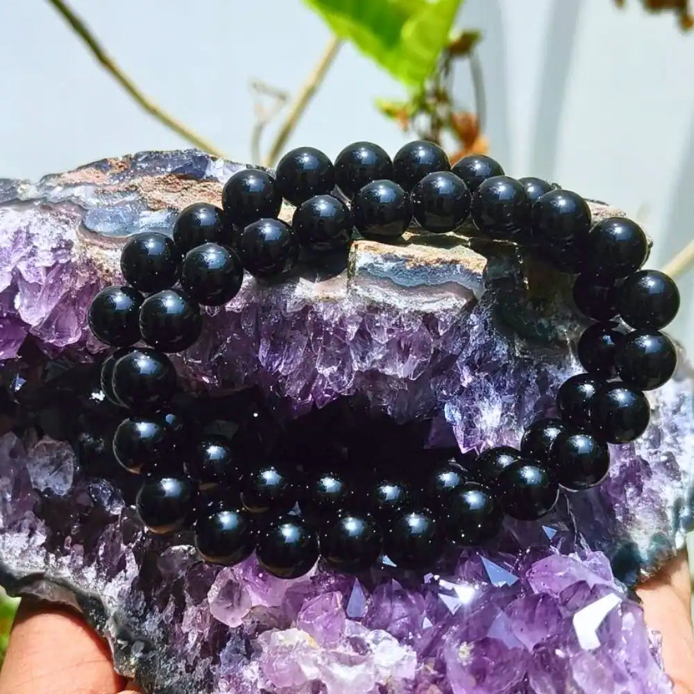 CRYSTCOP black obsidian bracelet made of polished round black beads displayed on a purple crystal geode