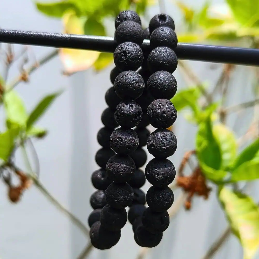 CRYSTCOP black lava bracelet with textured volcanic beads hanging outdoors on a black rod