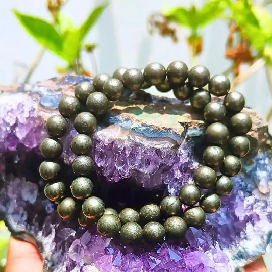 Golden pyrite bracelet made of round beads displayed on a purple crystal geode background