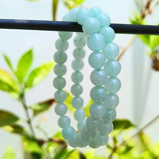 Green Aventurine Bracelet made of round polished beads hanging on a black rod with green foliage background