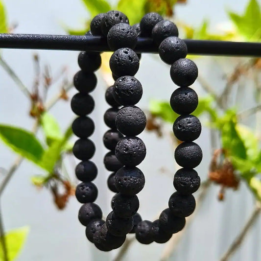 CRYSTCOP black lava bracelet with textured round beads hanging on a branch outdoors