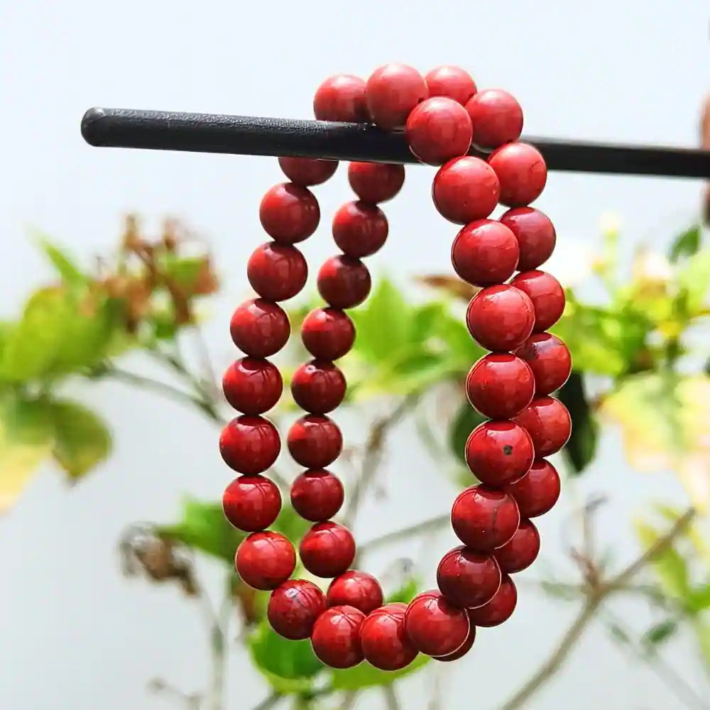 CRYSTCOP red jasper bracelet with polished round beads hanging outdoors with greenery background