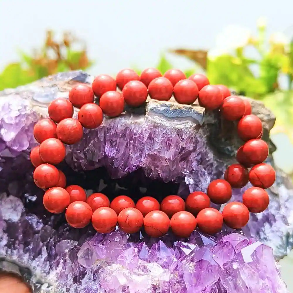 CRYSTCOP red jasper bracelet with polished round beads displayed on purple amethyst crystals