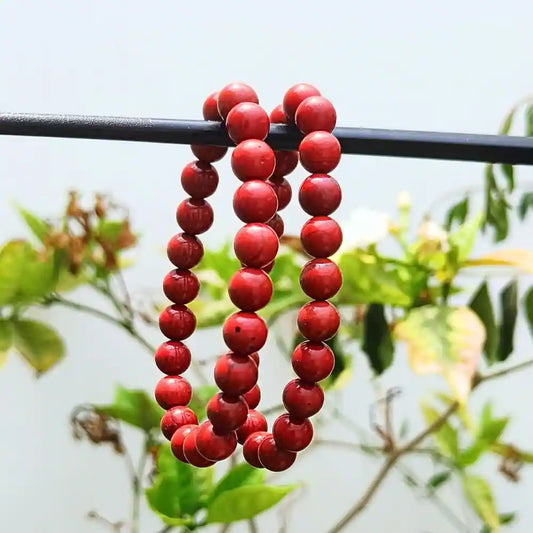 CRYSTCOP red jasper bracelet made of smooth round red beads hanging on a black rod outdoors
