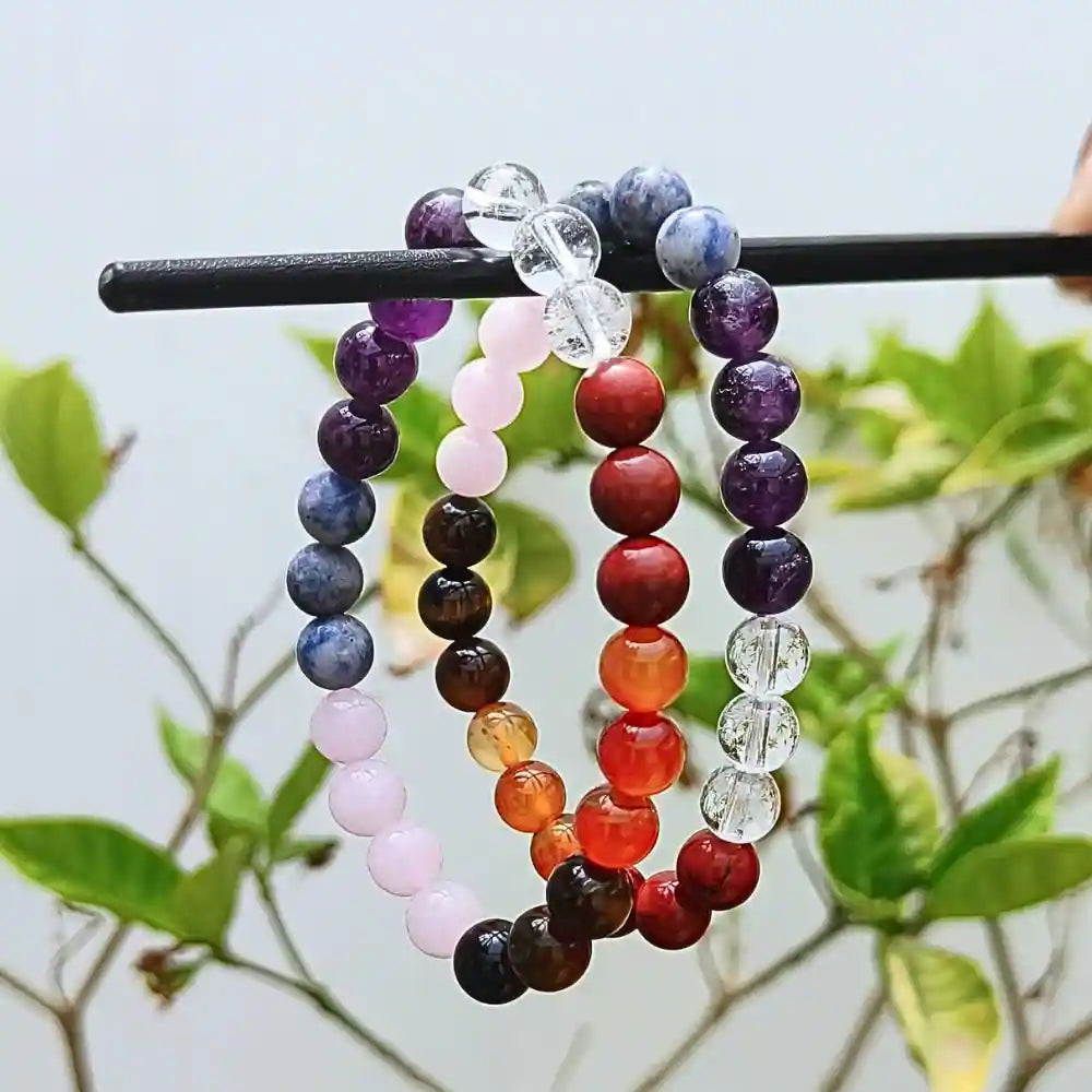 CRYSTCOP gemstone chakra bracelet featuring multicolored natural stone beads hanging on a black rod with green plants background