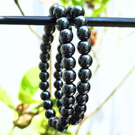 CRYSTCOP hematite bracelet 8mm with polished black beads hanging on a rod outdoors